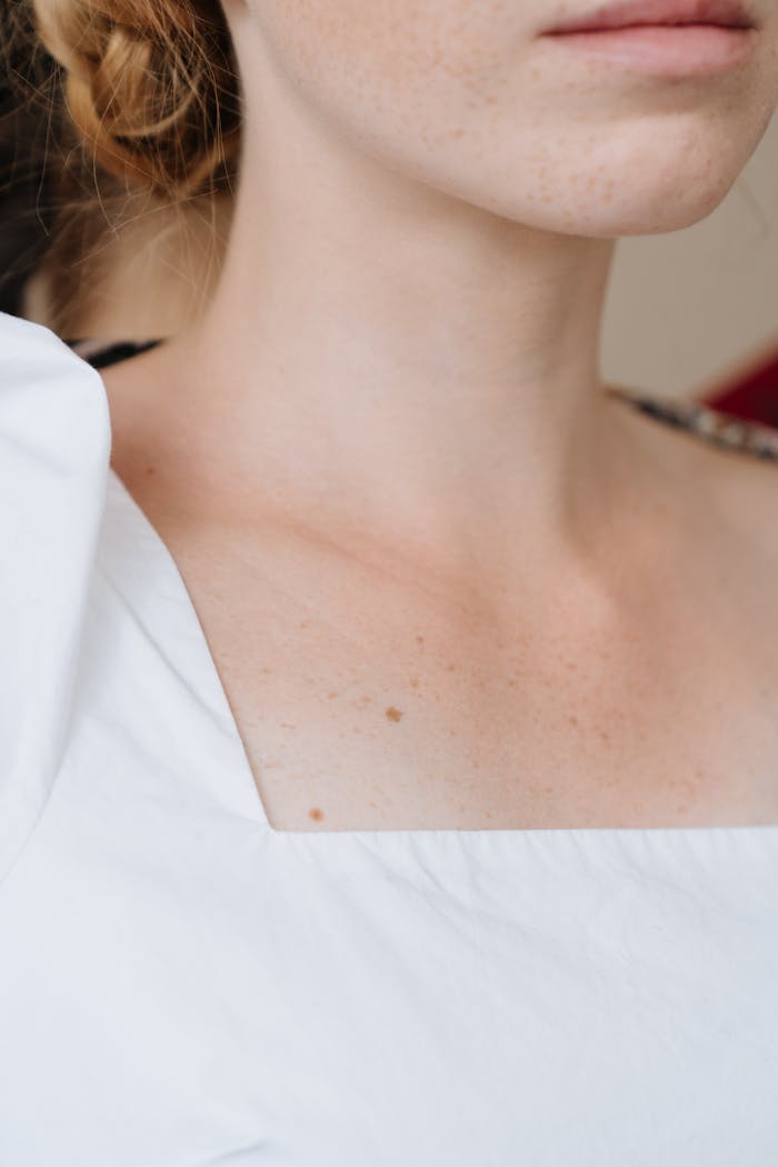 gallery-01 An intimate close-up of a woman's neck and shoulder in a white top, highlighting freckles and skin detail.